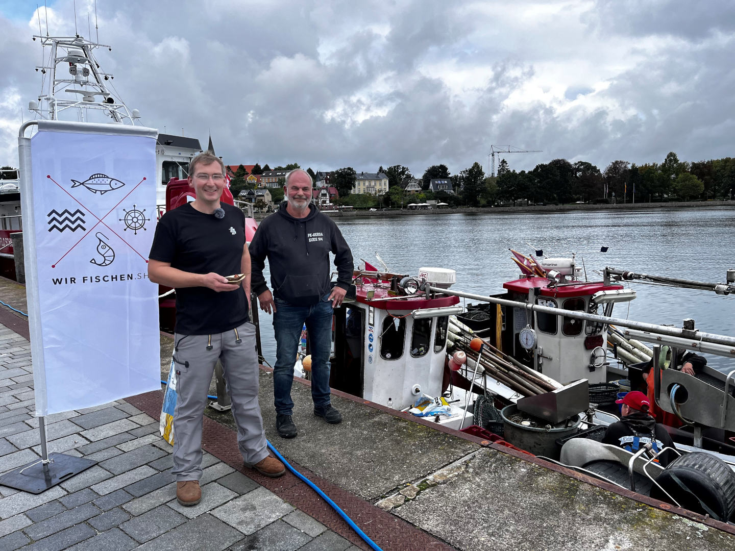 Zwei Männer stehen vor einem Schiff am Wasser 