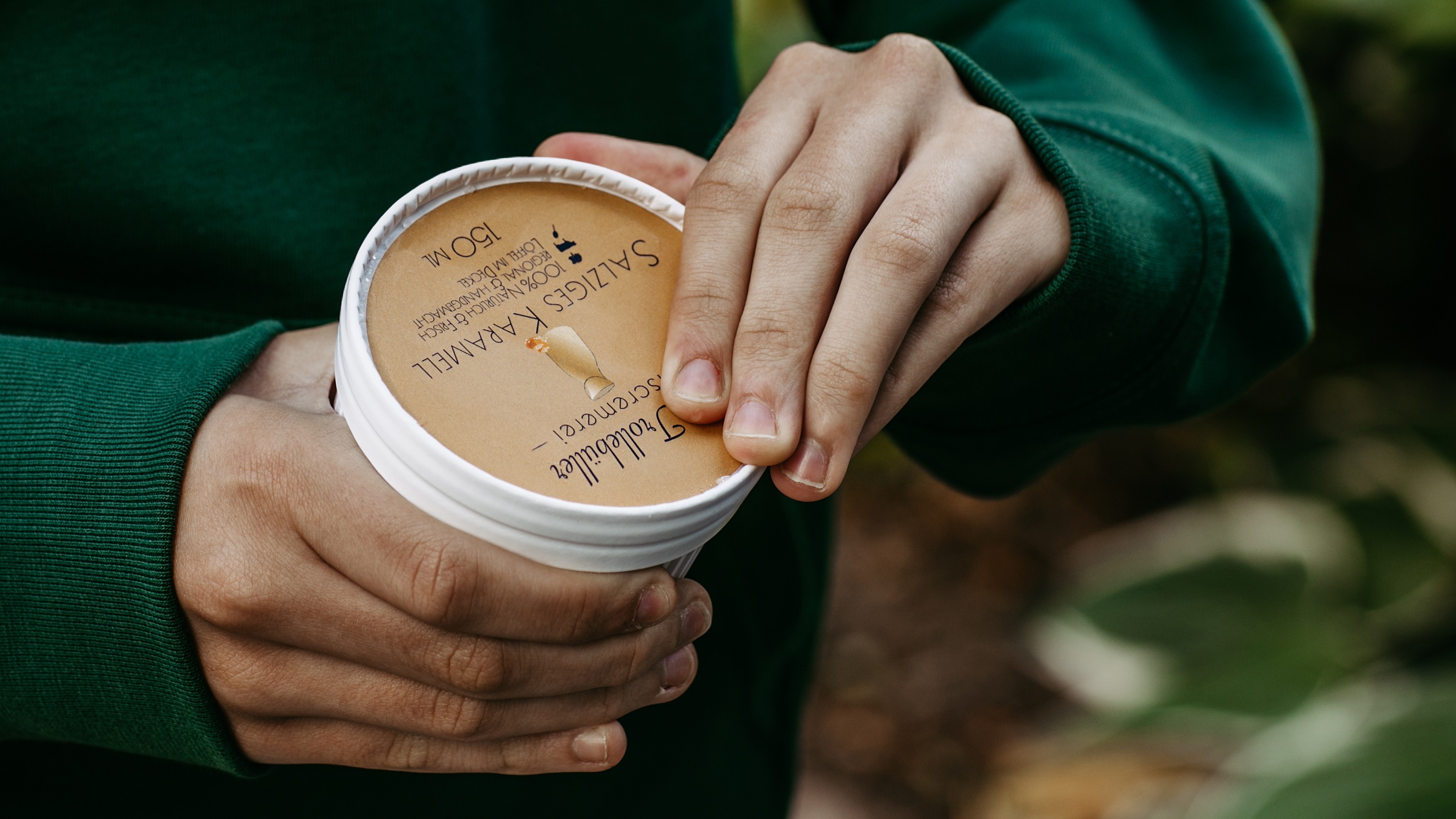 eine Hand hält einen Eisbecher fest, mit der zweiten wird dieser geöffnet