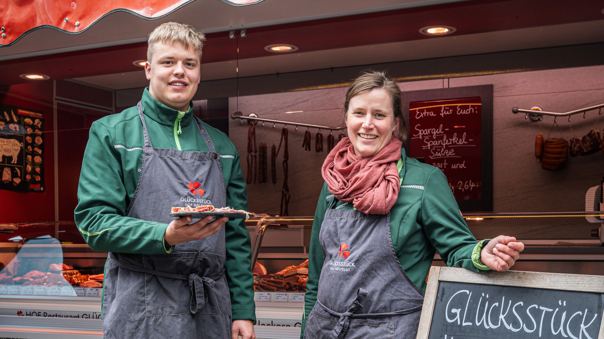 Ein Mann und eine Frau stehen vor einem Verkaufswagen und bieten Wurst zur Verkostung an