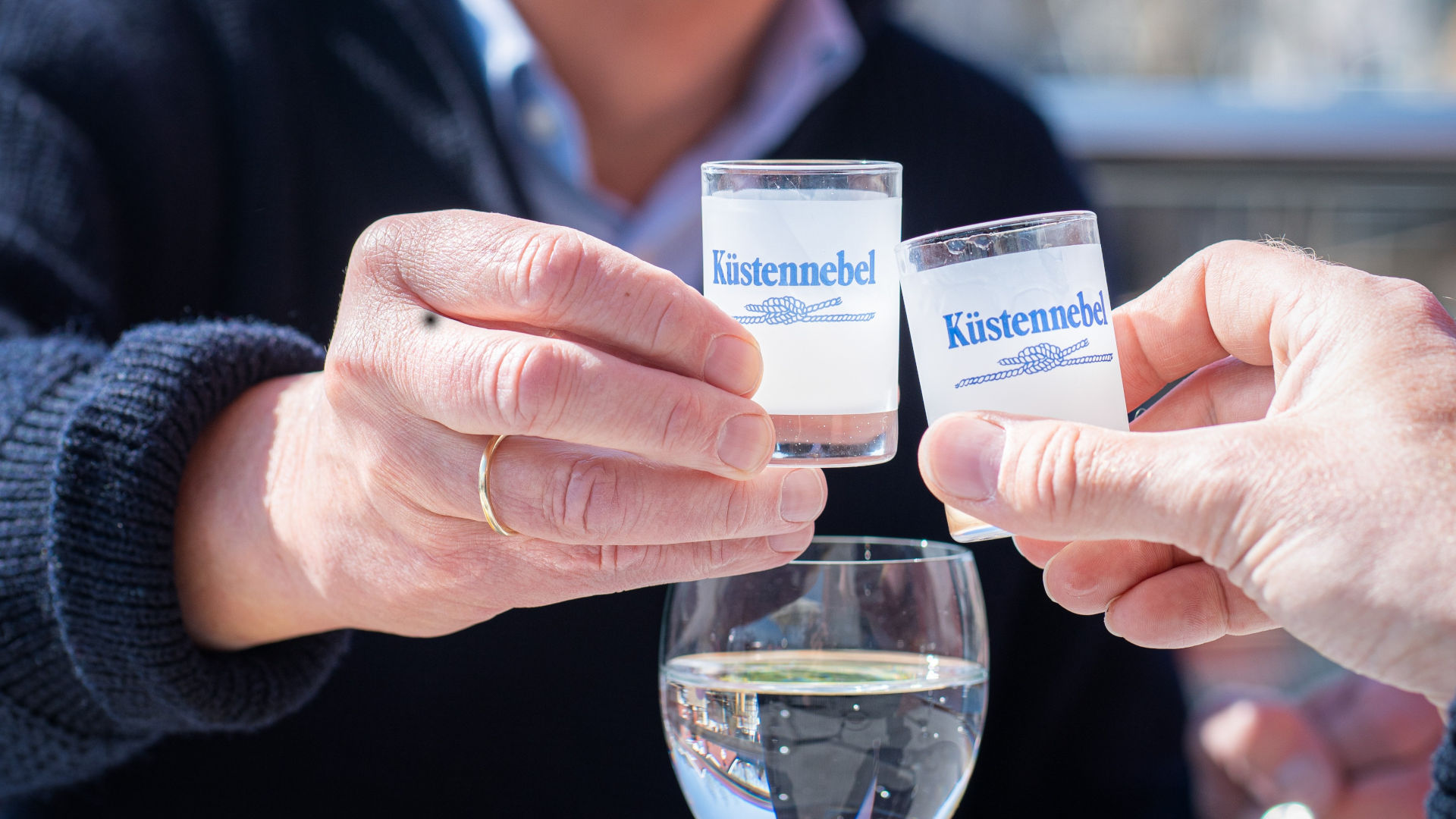 zwei Hände, die mit jeweils einem gefüllten Schnapsglas anstoßen