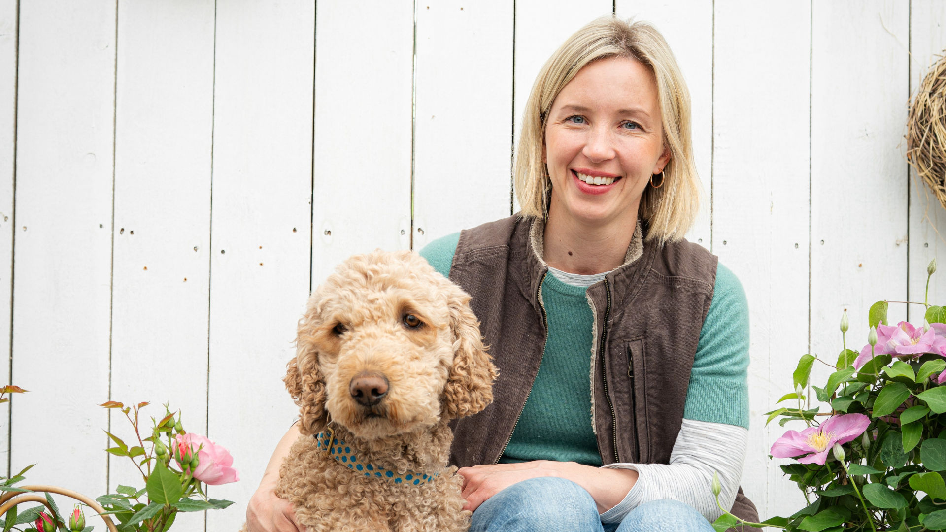 Blonde Frau lächelt in die Kamera, neben ihr ein Hund