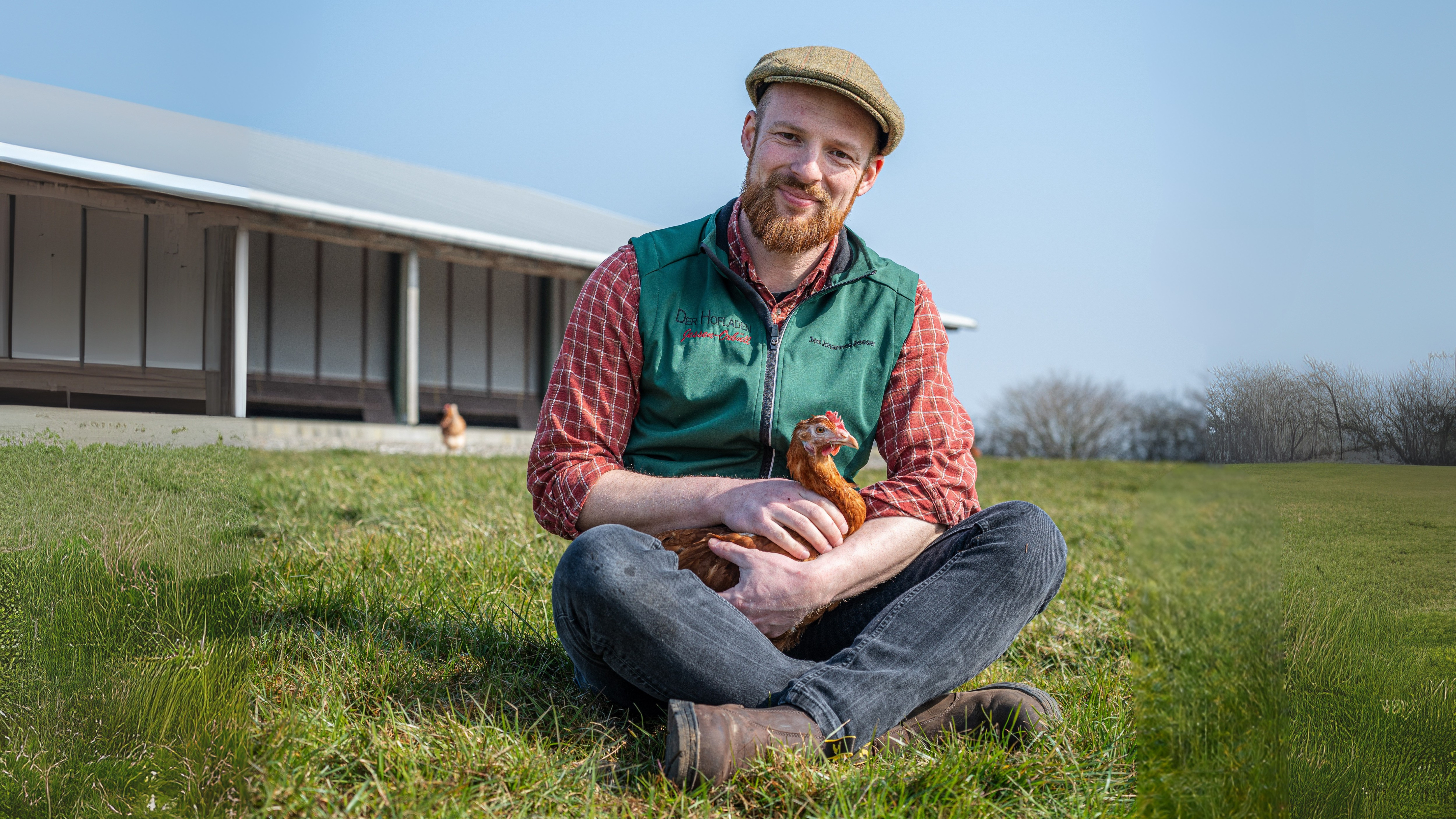 Mann sitzt auf der Wiese und hat ein Huhn auf dem Schoß
